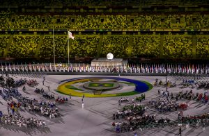 A foto foi feita em uma parte da cerimônia de abertura dos Jogos Paralímpicos de Tóquio. Há um tablado central no estádio com a bandeira e as cores do Brasil. Diversos atletas paralímpicos aparecem distribuídos no local.