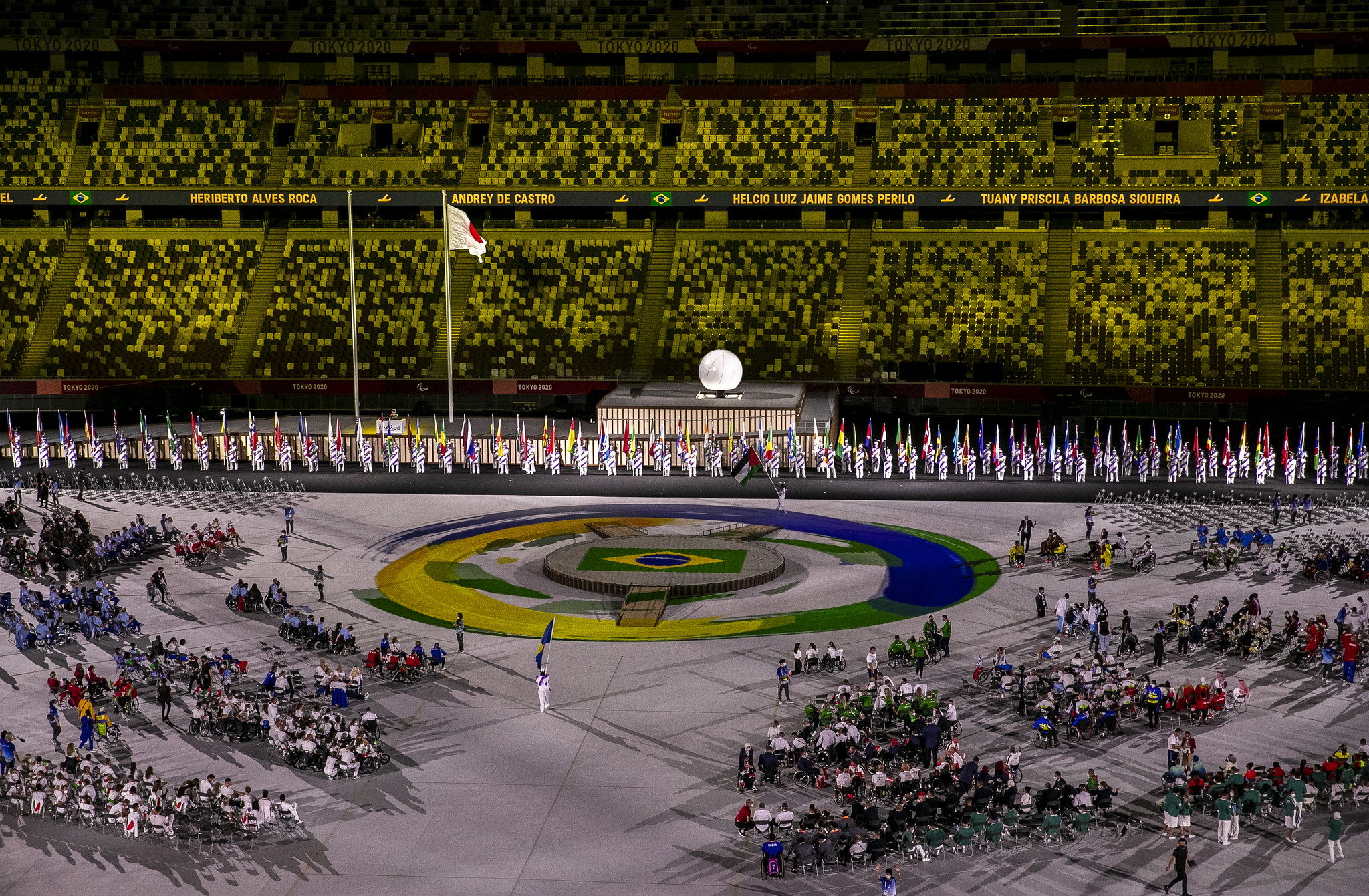 A foto foi feita em uma parte da cerimônia de abertura dos Jogos Paralímpicos de Tóquio. Há um tablado central no estádio com a bandeira e as cores do Brasil. Diversos atletas paralímpicos aparecem distribuídos no local.