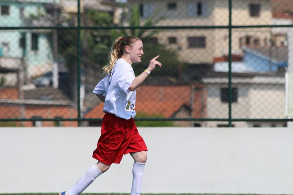 Imagem da jogadora Mariana Damásio de lado, do calcanhar à cabeça, caminhando no campo.