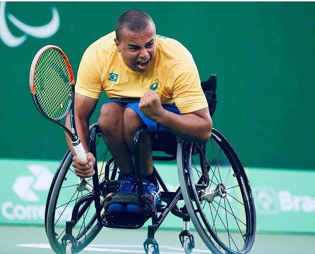 Fotografia do tenista Rafael Medeiros em que aparece na cadeira de rodas com o uniforme verde, amarelo e azul do Brasil e uma raquete na mão esquerda.