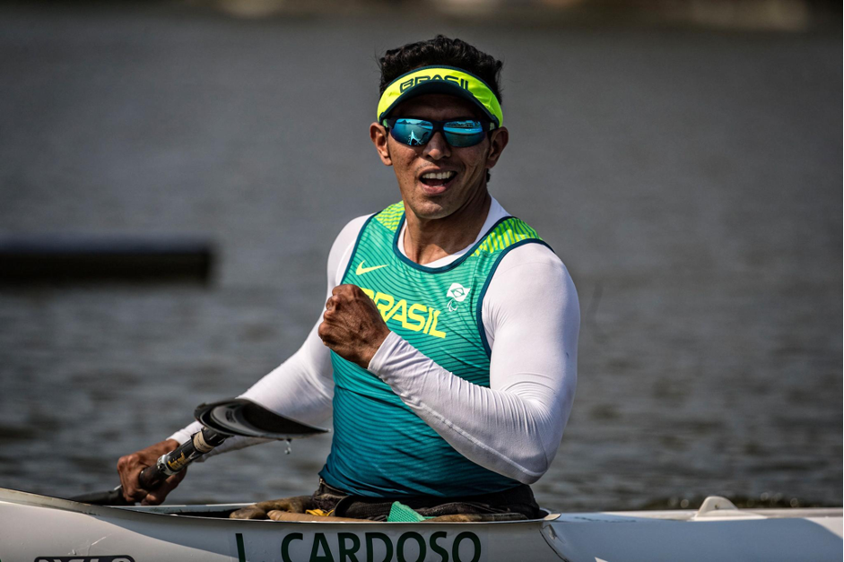 Atleta Luis Carlos Cardoso, homem pardo, usando uma blusa tipo segunda pele branca, com uma camiseta verde por cima, óculos escuros e um boné verde. Ele está sentado na canoa e segurando o remo com a mão direita (Foto: CPB) 