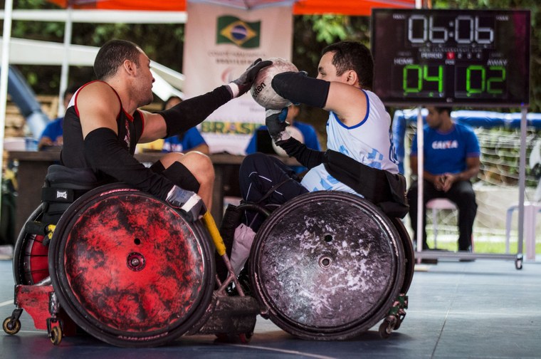 Foto mostra dois jogadores de rugbi sobre cadeiras de rodas disputando uma bola