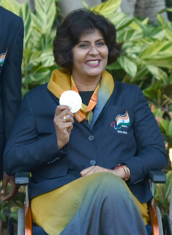 Deepa sorri enquanto mostra sua medalha, posando para uma foto.