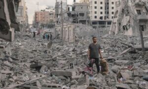 Homem Palestino em pé após bombardeio israelense na Faixa de Gaza. Foto: Motaz Azaiza