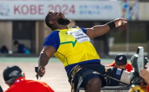 Homem negro com uniforme do Brasil e expressão de força durante prova de arremesso de peso F57
