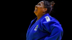 Judoca com kimono azul olha pra cima e sorri.